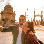 A happy couple taking a selfie in front of the famous liberty bridge during summer in Budapest in Hungary