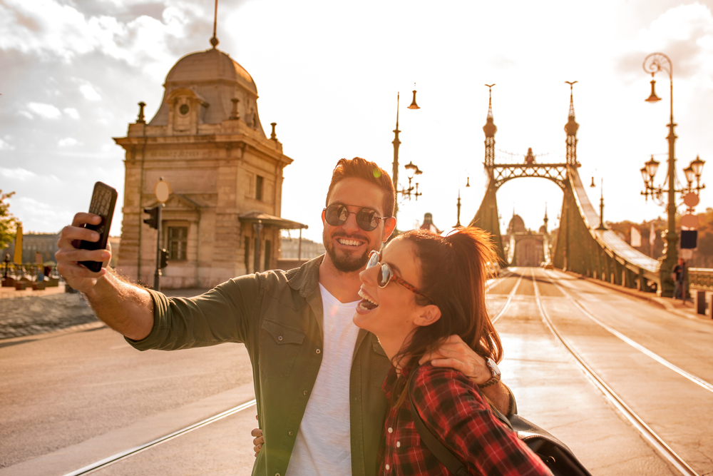 A happy couple taking a selfie in front of the famous liberty bridge during summer in Budapest in Hungary
